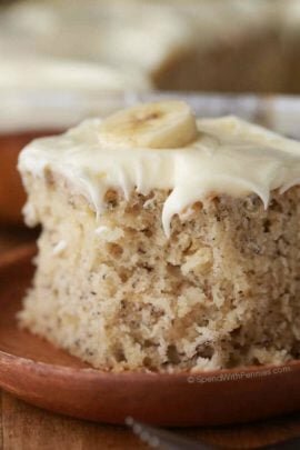 frosted banana cake with a banana on top on a wood plate