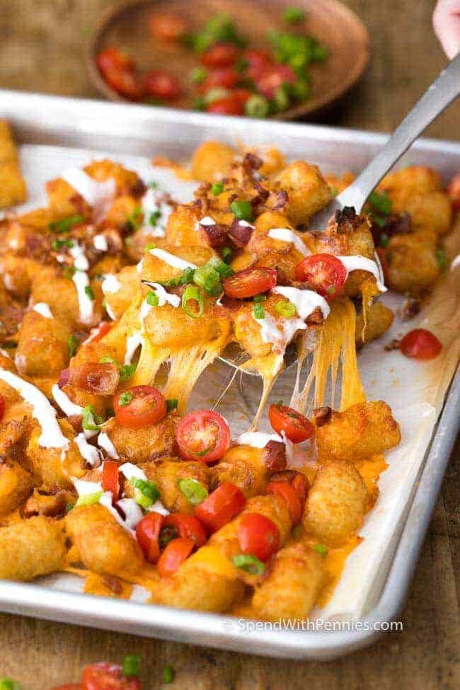 serving up Tater Tot Nachos garnished with green onion and tomatoes, from a baking tray