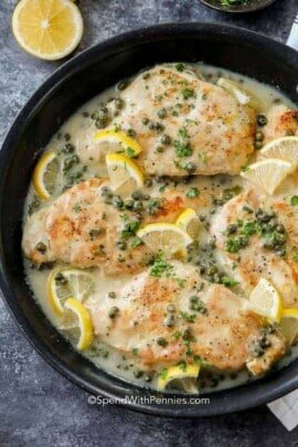 a skillet of chicken piccata garnished with lemon slices